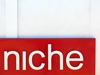 A red rectangular sign with the word 'niche' written in large white letters. The background is a plain off-white wall with a vertical white strip on the left side.