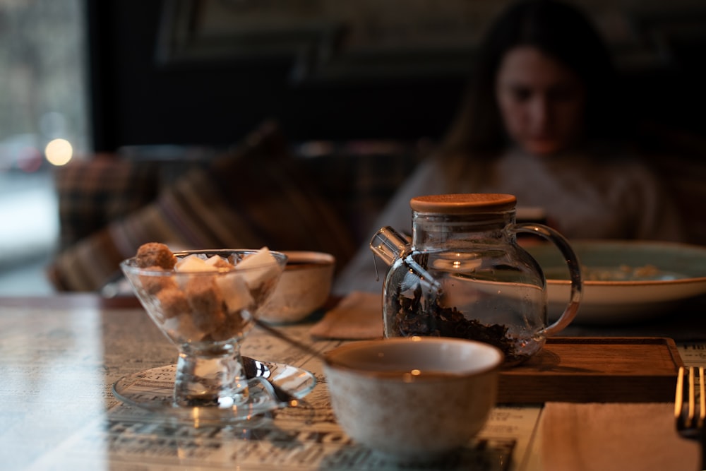 woman in black shirt sitting beside table with white ceramic bowl and clear glass pitcher