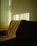 Sunlight filters through vertical blinds, casting striped shadows across a textured sofa in an interior space. The light creates a warm, inviting atmosphere with a play of light and shadow.