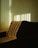 Sunlight filters through vertical blinds, casting striped shadows across a textured sofa in an interior space. The light creates a warm, inviting atmosphere with a play of light and shadow.