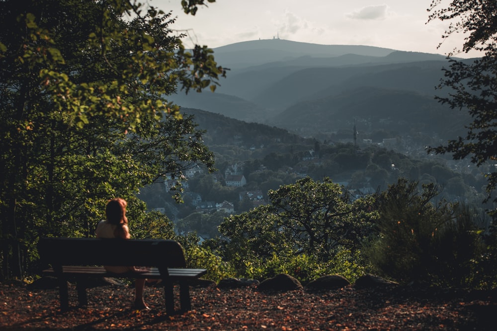uomo seduto sulla panchina che guarda le montagne durante il giorno
