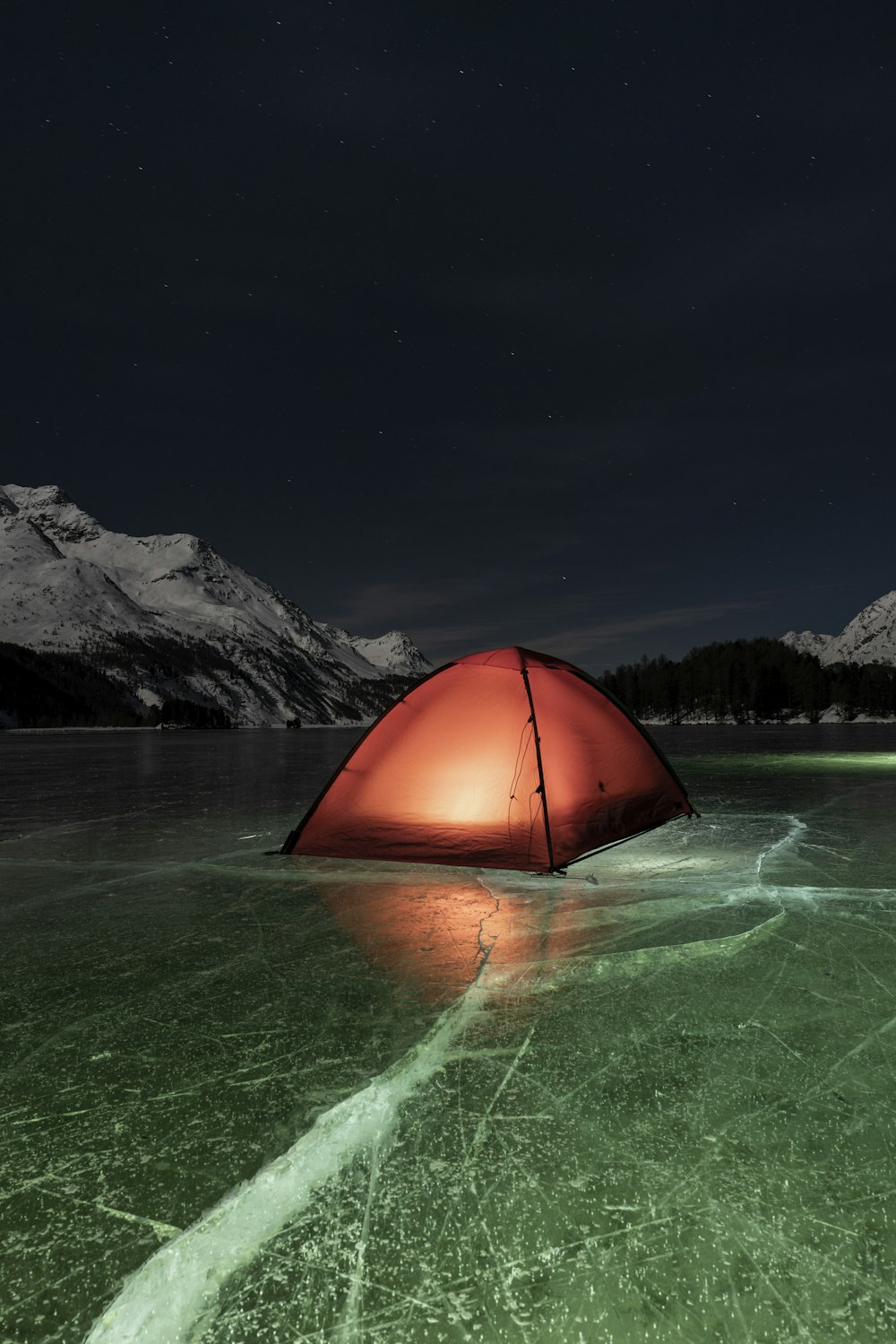 Tente dôme orange sur l’eau verte près de la montagne pendant la nuit