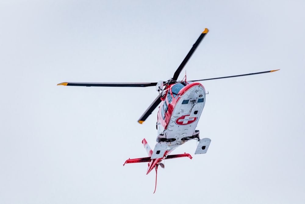 white and red helicopter flying in the sky