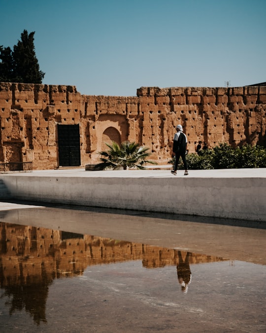 man in black jacket and black pants walking on gray concrete road during daytime in El Badii Palace Morocco