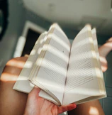 Close-up of hands holding an open novel with soft natural light streaming in.