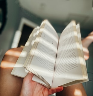 A cozy scene of a person reading a hardcover book titled ‘Restoration and Deliverance’ near a window with sunlight streaming in