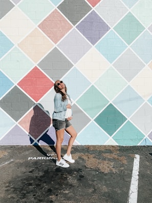 A young woman wearing a chic pastel blazer paired with trendy sneakers, standing against a city mural.