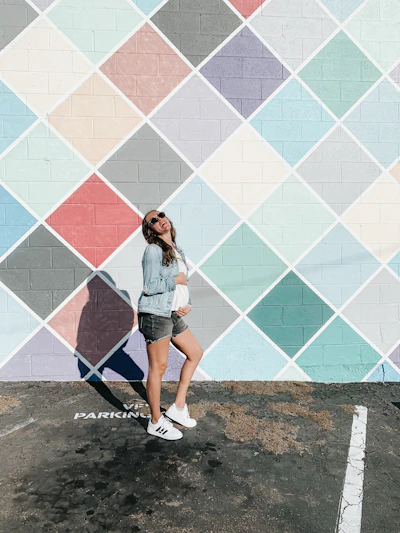A model wearing a vibrant sweatshirt standing against a colorful urban mural.