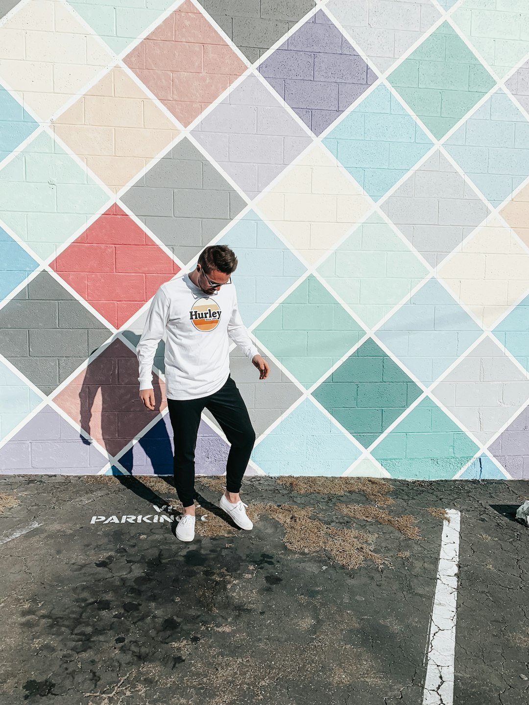 man in white crew neck t-shirt and black pants standing beside blue and white wall