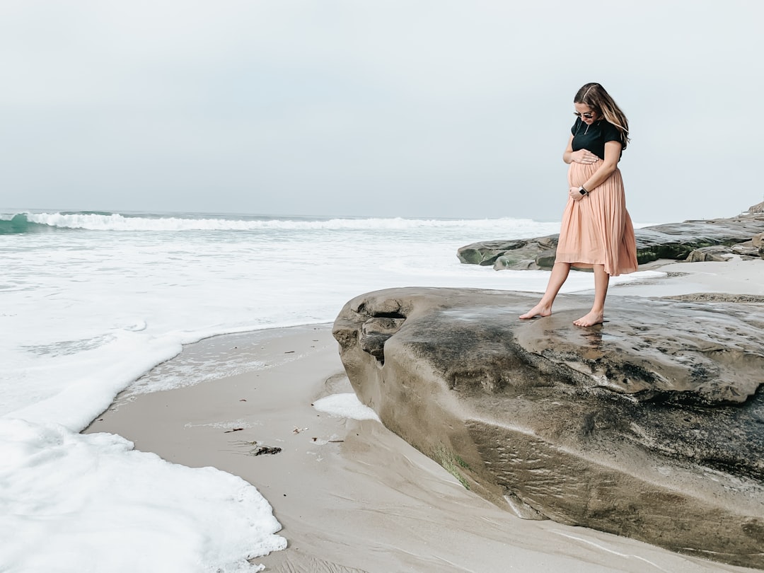 woman in orange dress standing on rock by the sea during daytime