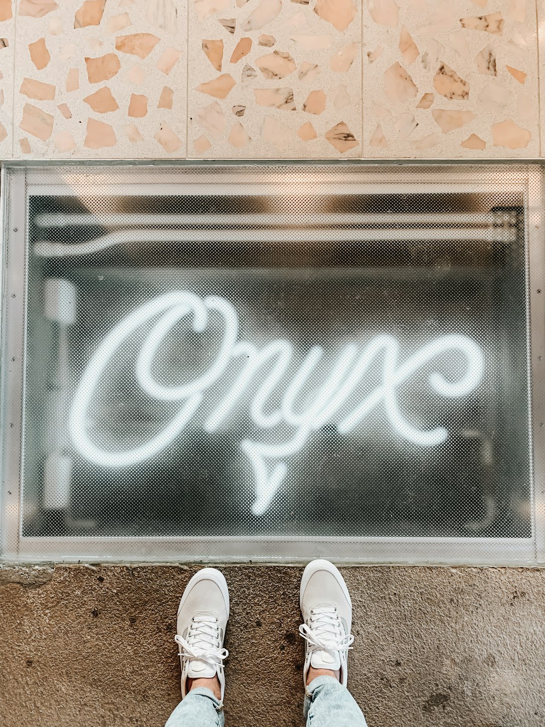  person wearing white sneakers standing on gray metal framed glass door doormat