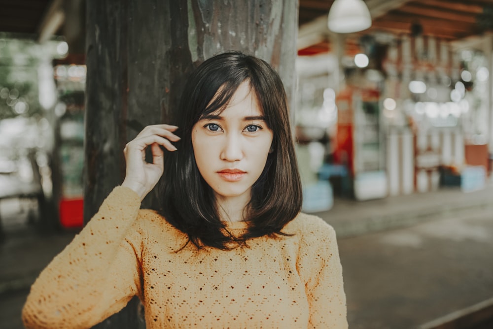 woman in orange long sleeve shirt standing beside black wooden wall during daytime