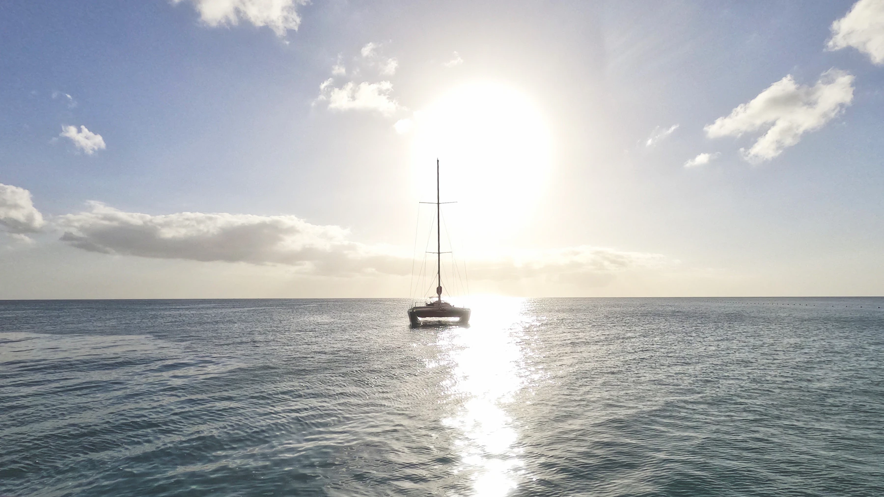 Catamaran on open water beneath a bright low sun