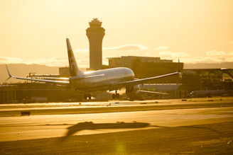 A sleek aircraft taxiing on a runway at sunset with control tower in the background.