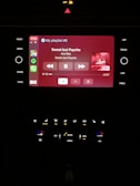 A car infotainment system displaying music information. The screen shows a currently playing song titled 'Sweet but Psycho' by Ava Max, with playback controls visible below the track information. The interface includes various app icons on the left, and temperature and audio controls below.
