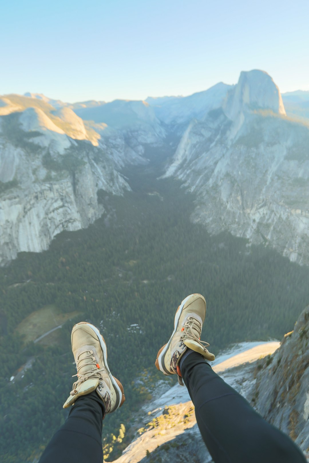 person in black pants and white sneakers sitting on rock mountain during daytime