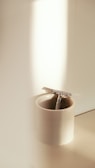 A metallic razor placed inside a white ceramic cup, illuminated by soft natural light from the side.