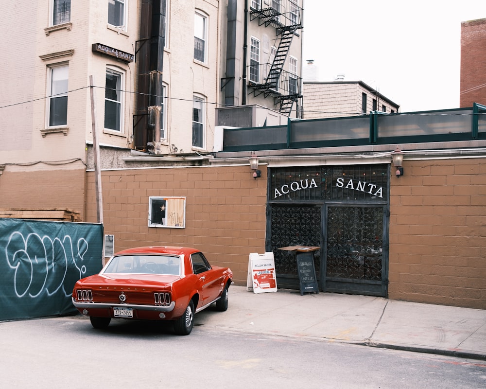 red coupe parked beside brown concrete building during daytime