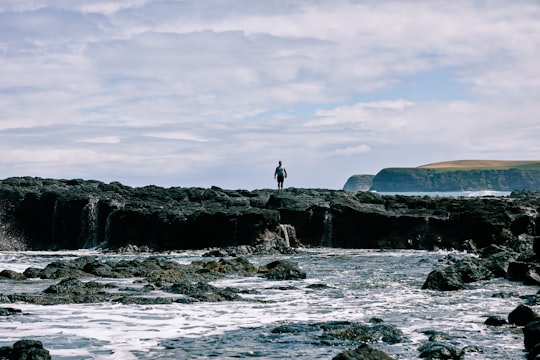 2 person standing on rock formation near sea during daytime in Mornington VIC Australia