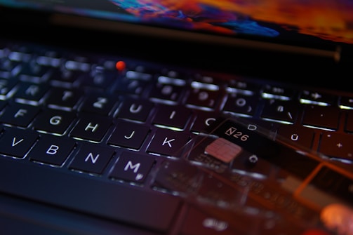 A close-up view of a keyboard with a focus on the keys. A transparent card with the text 'N26' is positioned on the keyboard, indicating a digital or banking theme. The lighting creates reflections and highlights that add a modern and technological feel.