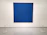 A large, textured blue canvas is mounted on a white gallery wall. Small, evenly spaced perforations create a subtle pattern across the surface. The artwork is cordoned off by a simple barrier with thin ropes attached to white circular stands on the floor.