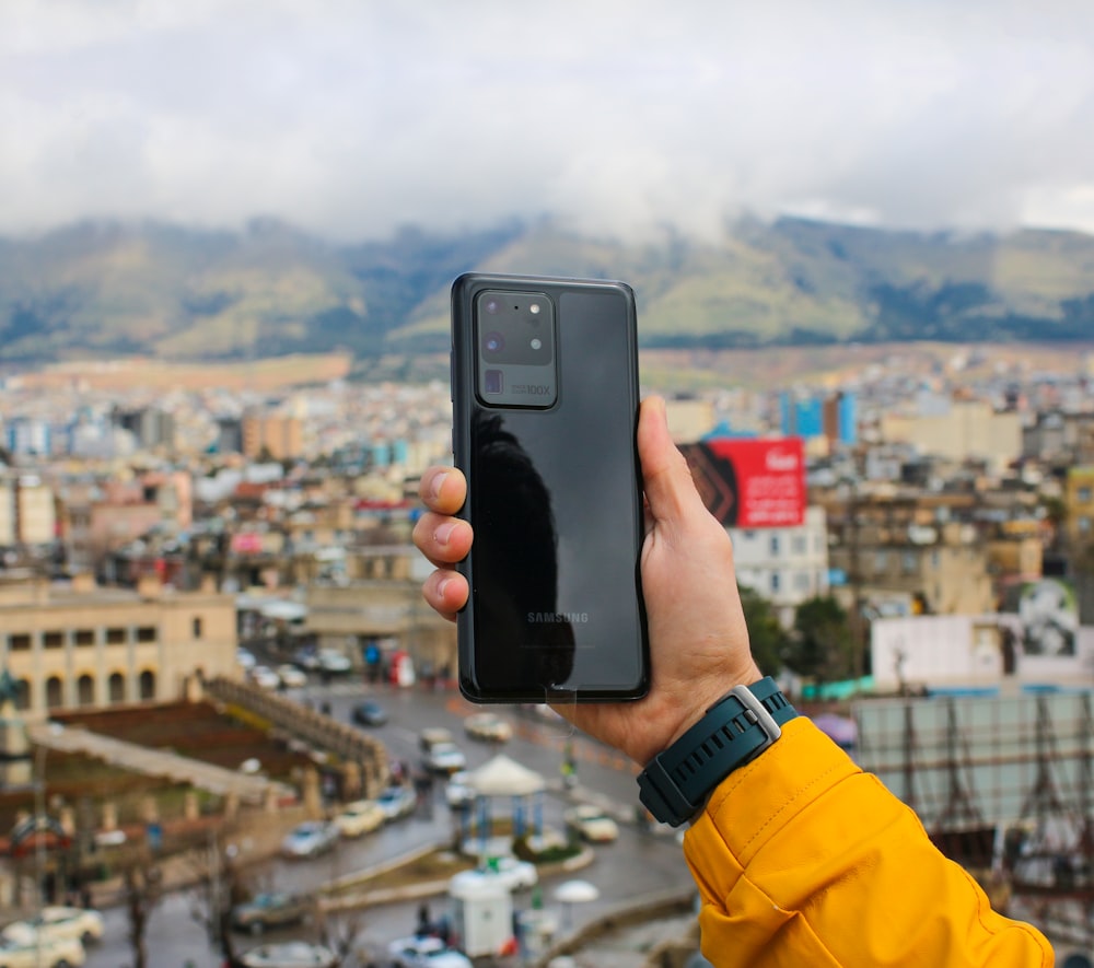 黒いスマートフォンを手に、昼間の街の建物の写真を撮る人