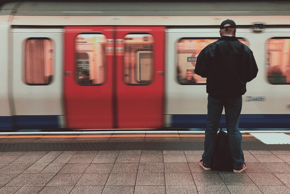 man in black jacket standing beside red train