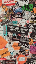 A collage of various colorful stickers layered over each other. The stickers have diverse themes including music, activism, brands, and art. Some include phrases like 'Love Obstbrand Hate Racism' and 'Feminist Pursuits'. The composition is vibrant and chaotic, featuring a mix of typography and graphic designs.