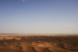 A vast desert landscape with rolling sand dunes under a clear blue sky.