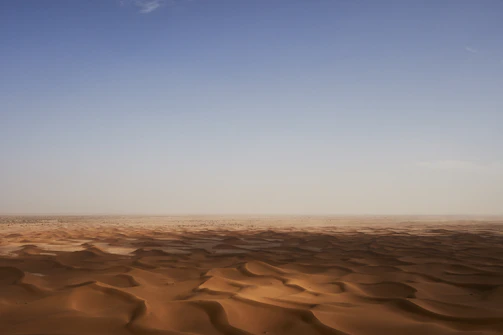 A vast desert landscape with rolling sand dunes under a bright blue sky.