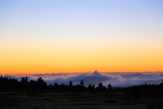 A serene landscape featuring a minimalist sunset with warm orange hues and soft gray clouds.