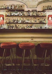 Cozy bar corner with warm lighting and rustic wooden shelves filled with bottles.