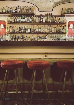 Cozy bar corner with warm lighting and rustic wooden shelves filled with bottles.