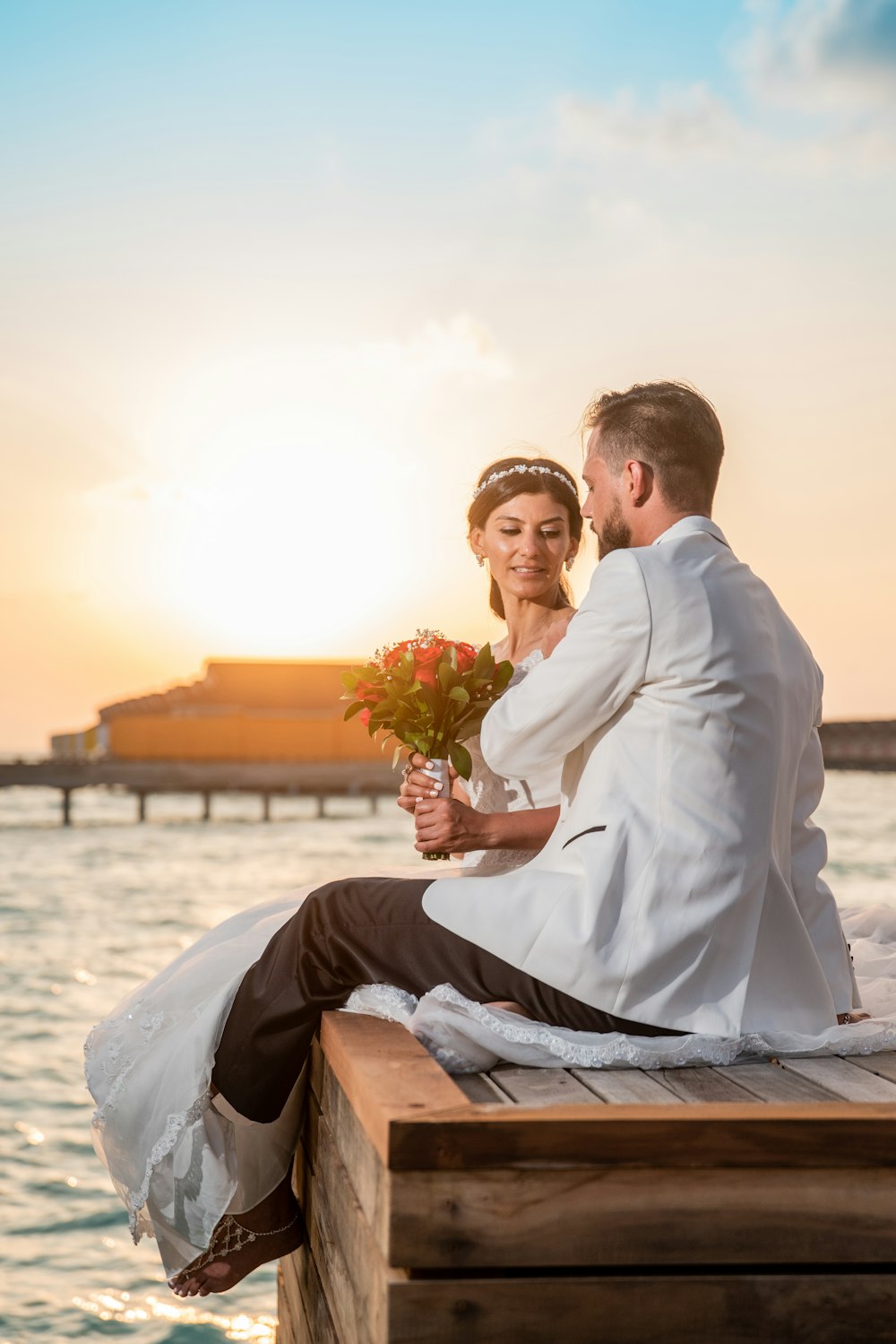 man in white suit sitting beside woman in white dress holding bouquet of flowers