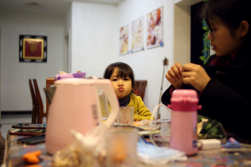 a little girl sitting at a table with a woman