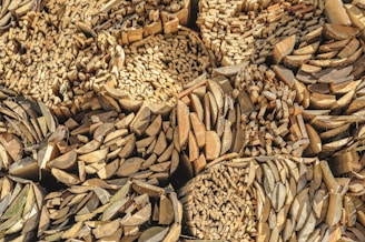 A large stack of cut and split firewood arranged in a tightly packed pattern. The logs are arranged in circular and grid-like formations, creating a visually interesting texture with different shades of brown and beige.