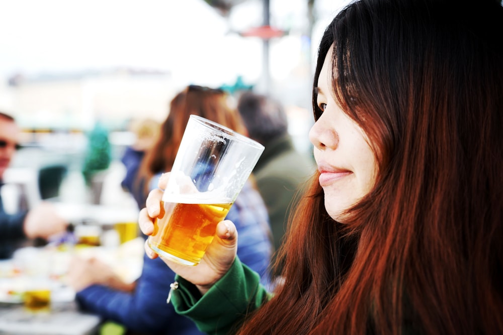 woman in green long sleeve shirt holding drinking glass with yellow liquid