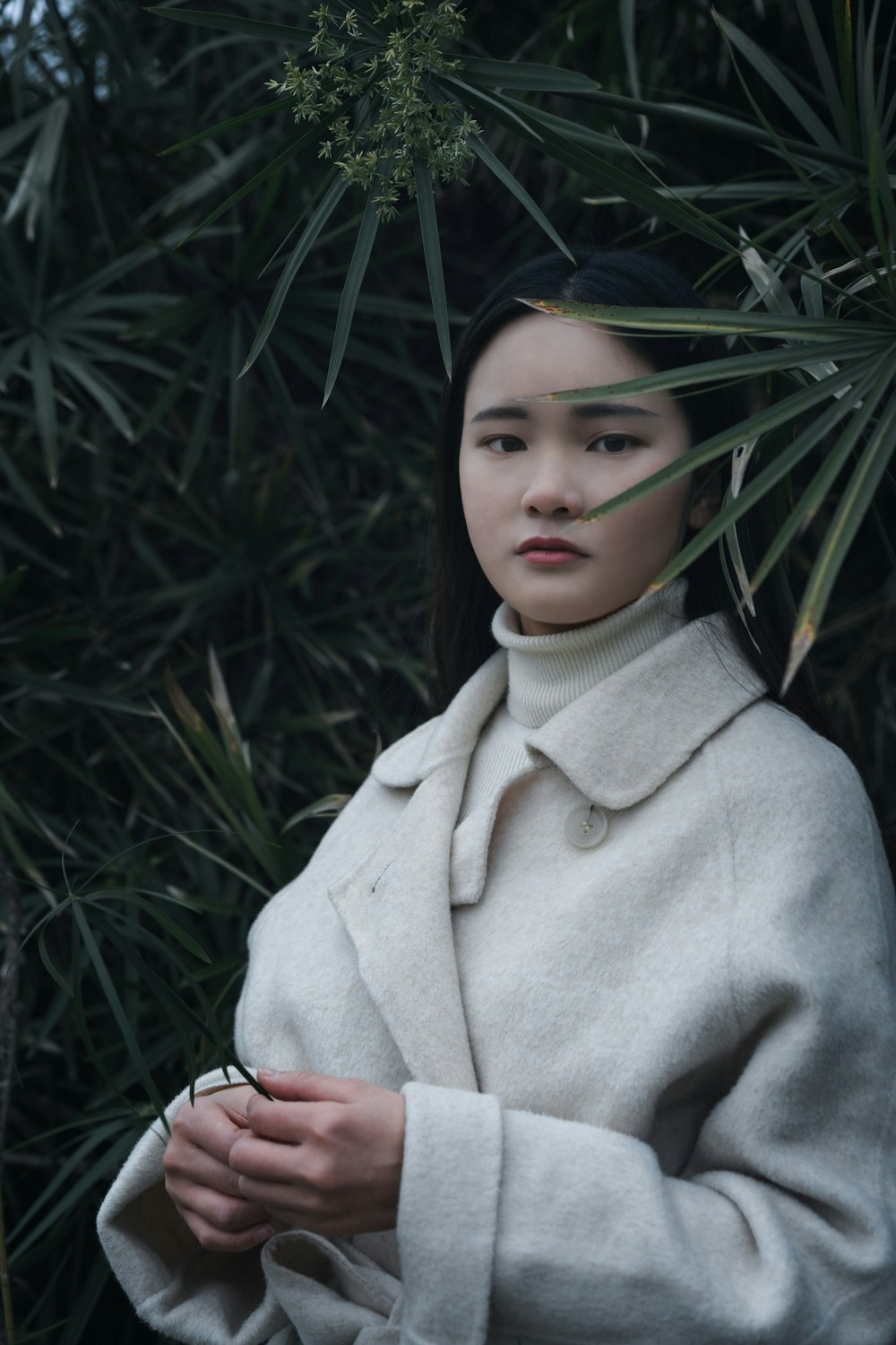 girl in beige coat standing near green plant