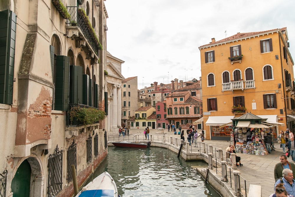 people walking on sidewalk near river with boats during daytime