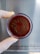 A gloved hand holds a petri dish with a red medium inside, featuring a playful drawing of a smiling face using a dark substance.