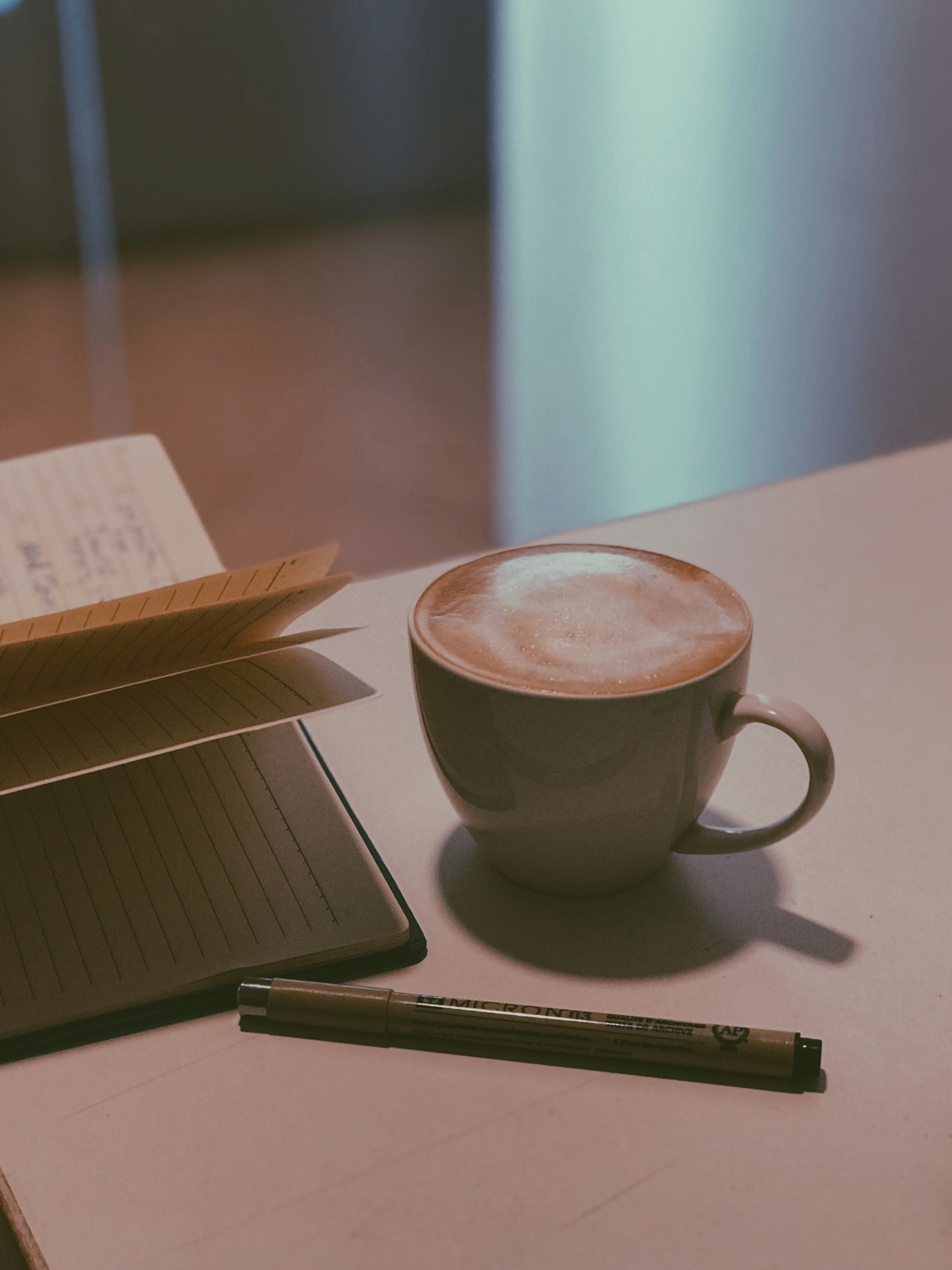 Open notebook and pen beside a cup of coffee in a bright, warm, natural daylight study environment — clean and editorial