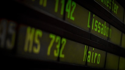Departure board displaying flight information with destinations such as Lissabon and Kairo in bright green digital text over a dark background.
