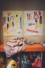 a couple of paintings on a wall above a shelf