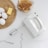 A kitchen scene featuring a white electric hand mixer surrounded by a wooden board with three eggs and a rectangular piece of butter. A pile of toasted bread is placed on a plate nearby, and there are mixer attachments scattered on the white countertop.