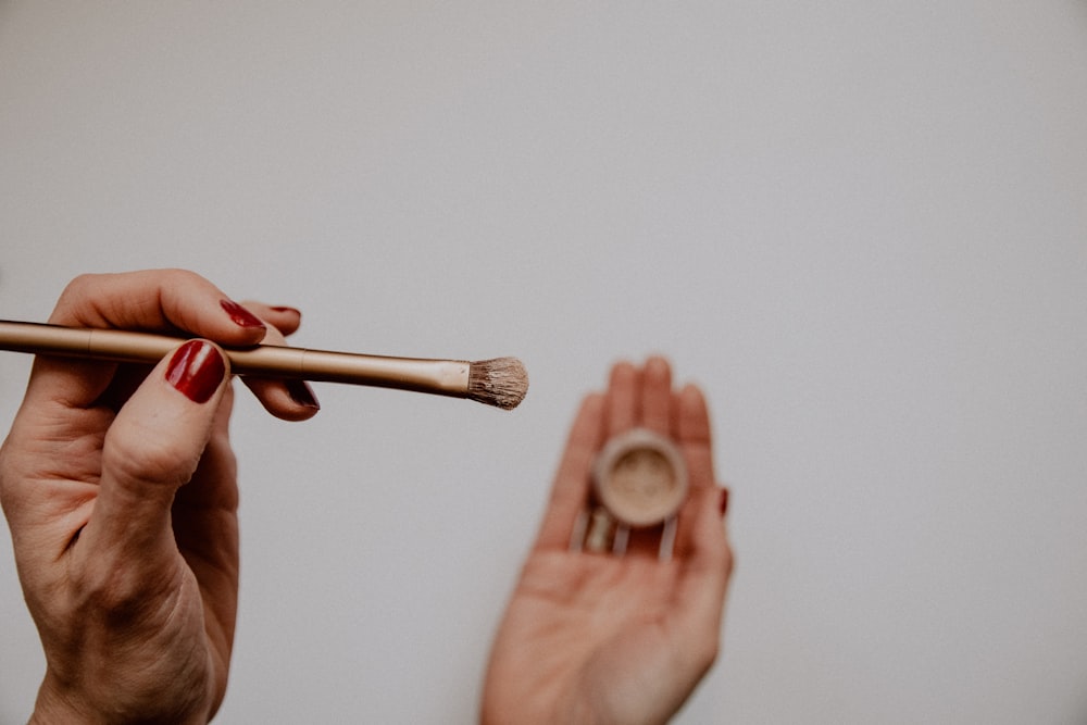 Persona sosteniendo una brocha de maquillaje marrón y blanca