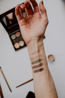 Vibrant makeup palette swatched on a hand with gold rings and soft sunlight.