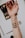 An extended arm with makeup swatches on the inner forearm. The swatches are in earthy tones, including shades of brown and green. A makeup palette and a brush are visible in the background.