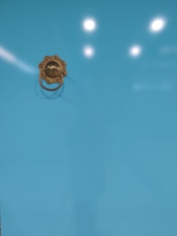 A bright turquoise surface with a brass door knocker attached, reflecting light from above.
