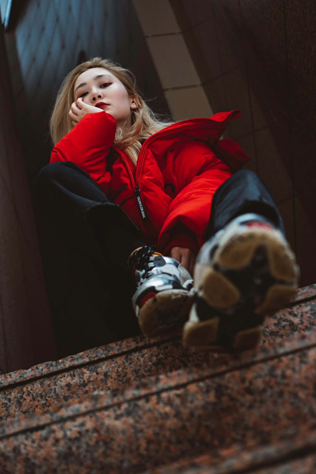 girl in red jacket and black pants sitting on brown concrete stairs
