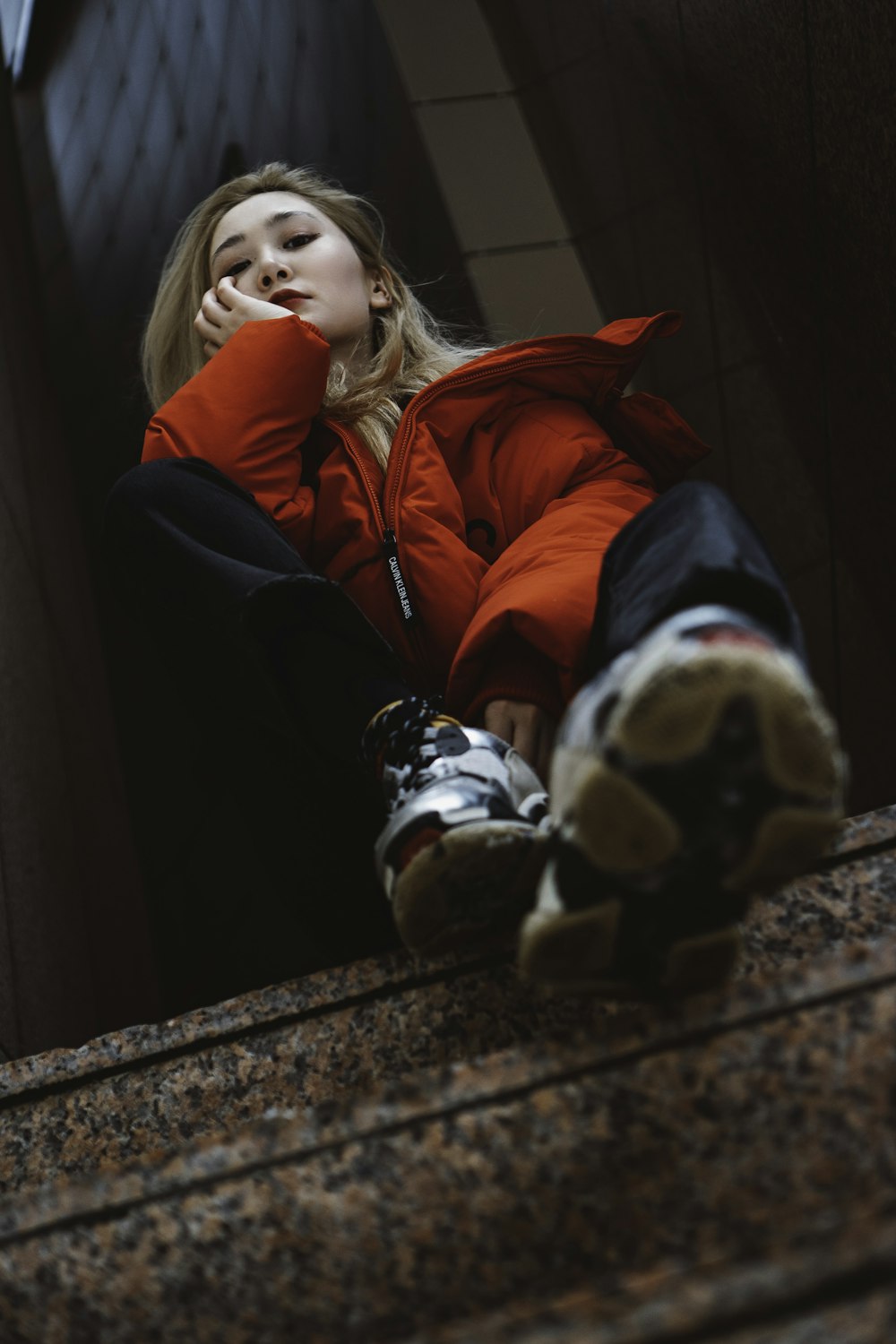 girl in red jacket and black pants sitting on brown concrete stairs
